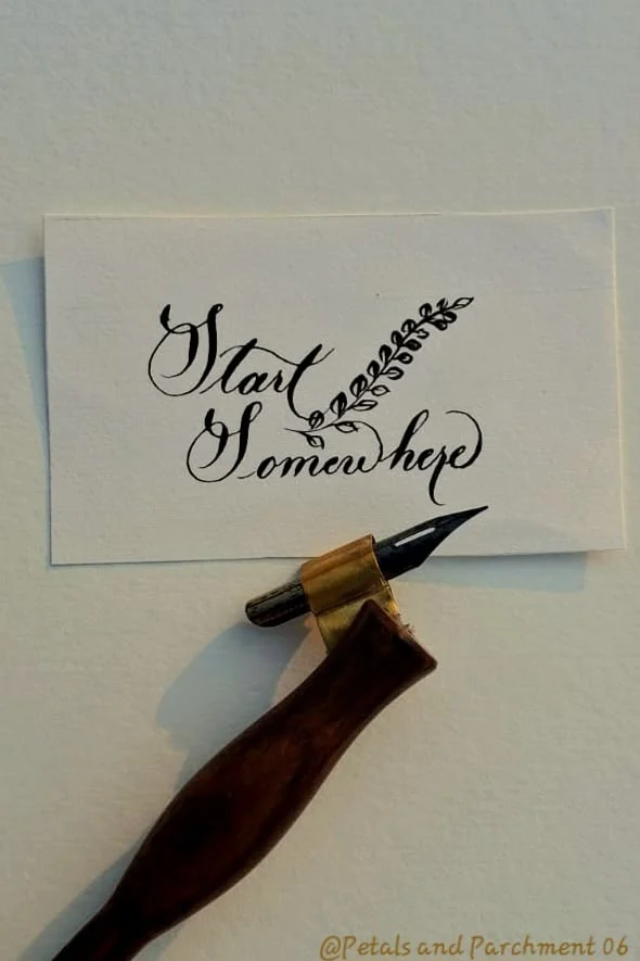 Pointed dip pen beside a Start Somewhere ink lettering card with delicate flourishes.